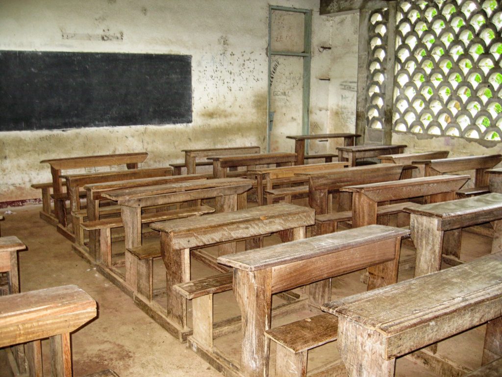 empty traditional classroom with dusty chalkboard beside a bright laptop on the desk – illustrating traditional education limits